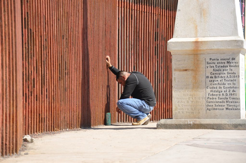 Man says goodbye to his partner through the US-Mexico border fence.